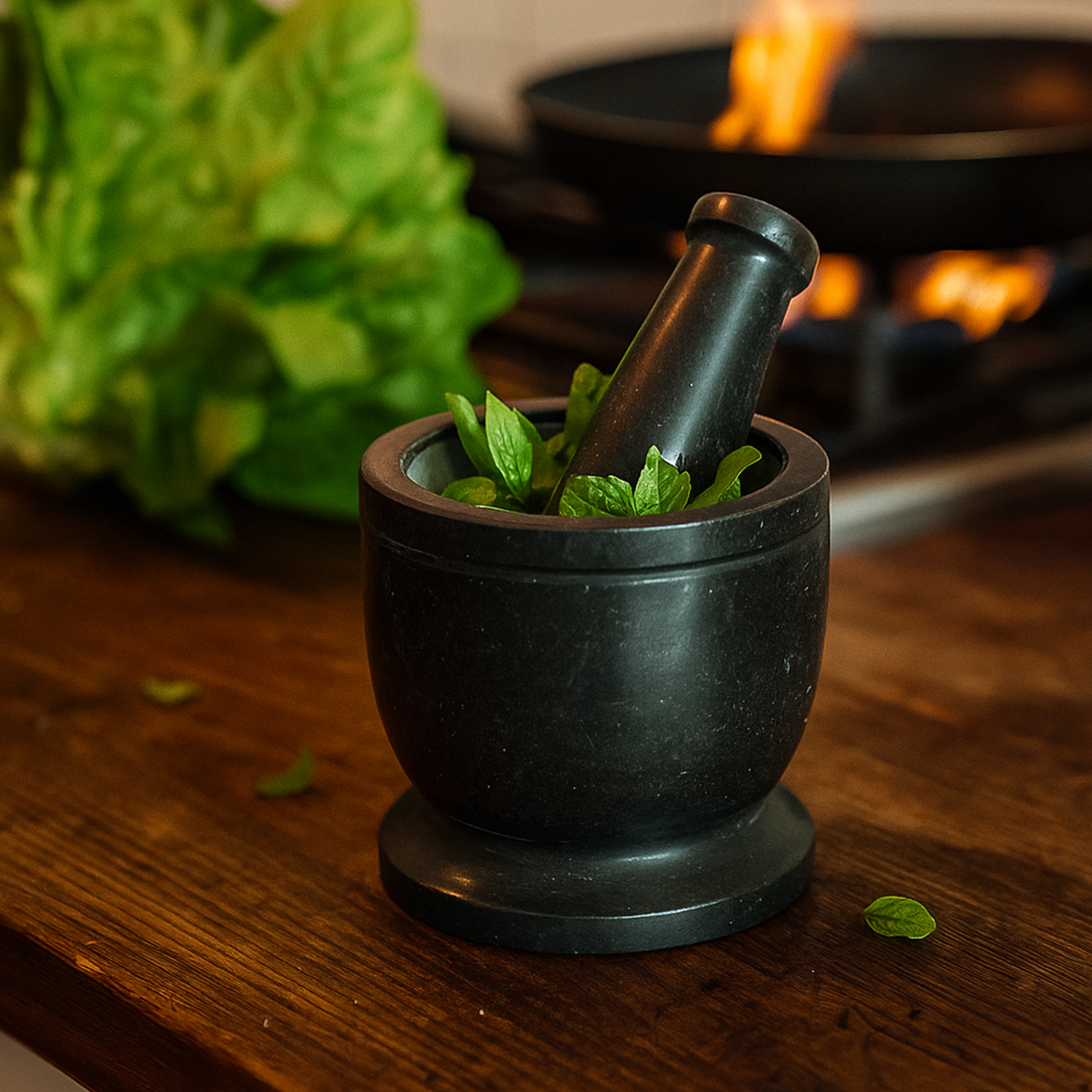 Black marble mortar and pestle with green herbs on a wooden surface, stove in the background