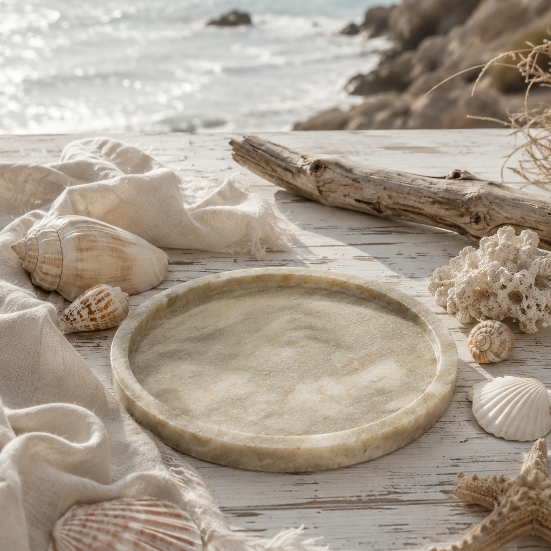 Luxury round beige marble tray styled on a beach with seashells, driftwood, and soft coastal decor.