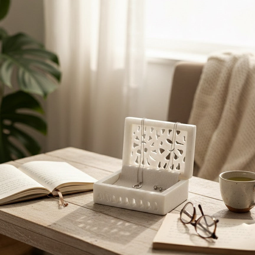 Marble jewelry organizer box with hanging loops sits open on a rustic wooden table in a softly lit room. 